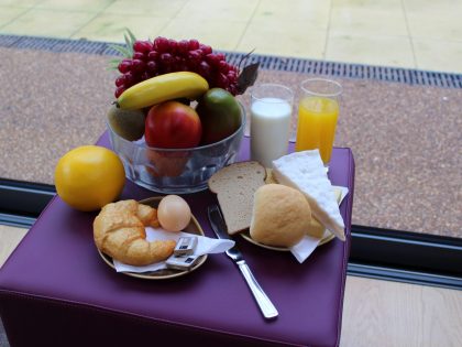 A small table set with a balanced breakfast including fruit, bread, croissant, cheese, juice and milk by a window