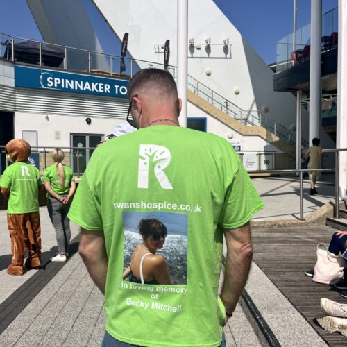 man stood facing away from camera wearing green t shirt for rowans hospice with picture of his late wife on the back stood in the sun infront of spinnaker tower in portsmouth