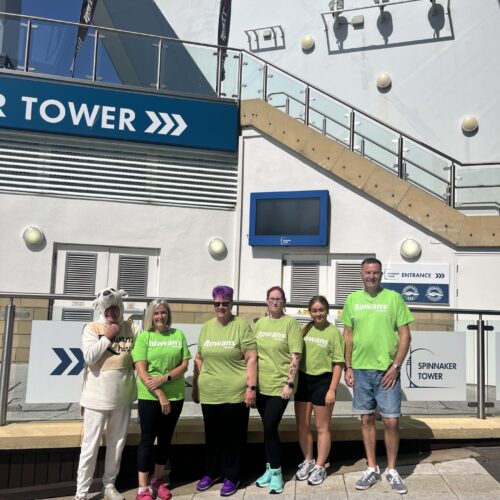 group of people wearing green rowans hsopice t shirts and an elderly lady in a polar bear costume stood together infront of the spinnaker tower for a photo before an abseil
