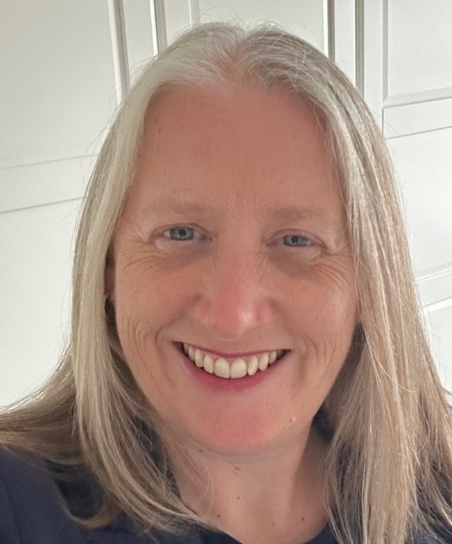 Headshot of woman smiling to camera. She has blue eyes and light blond hair.