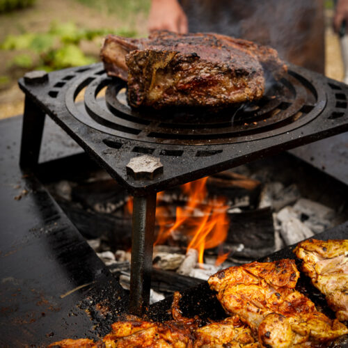 close up of grill on fire with big piece of meat cooking.