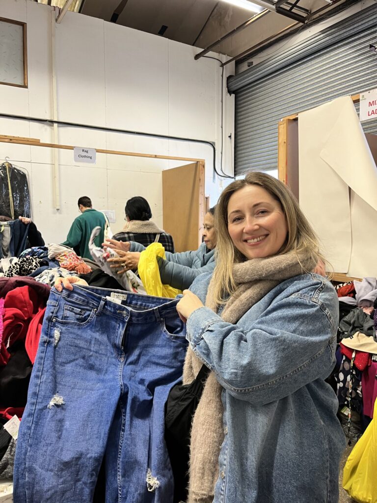 woman in scarf and jacket holding up jeans and clothes at a jumble sale