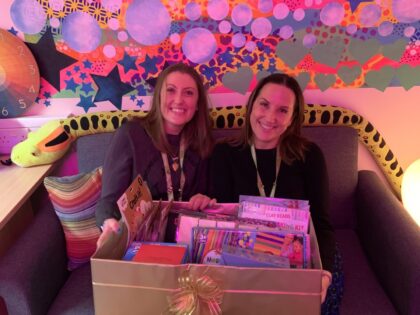 colourful room with toys and two people holding a box of art and crafts on a sofa