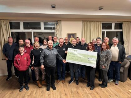 large group of men and women holding a cheque presentation indoors