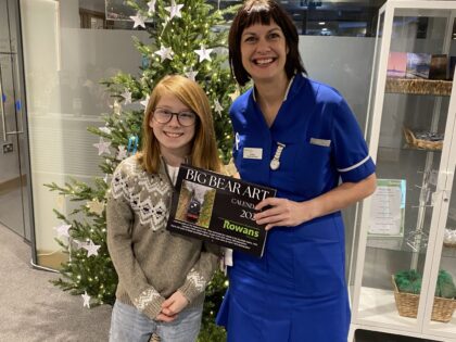 nurse and small boy holding a calendar infront of a christmas tree