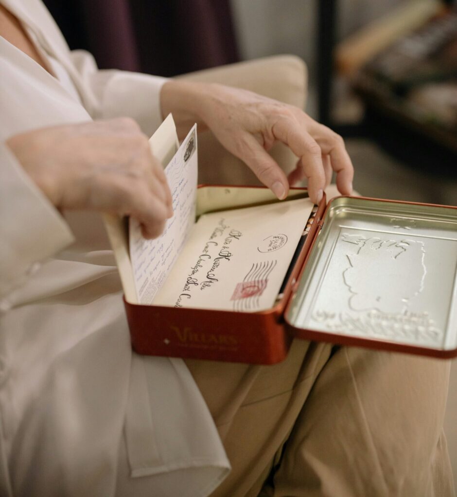 image focused on the hands of a lady and a red tin on her lap going through old letters in her living room and she has reading glasses on
