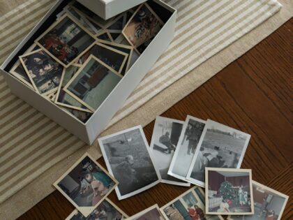 a top view of a cardboard box with old family photos in laid on a table with a cream cloth