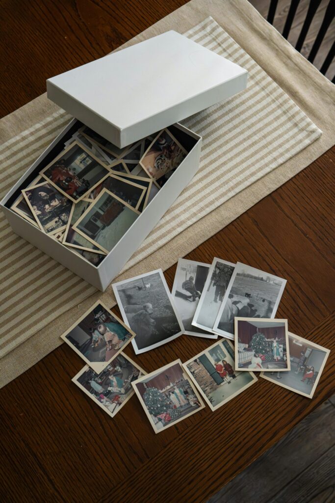 a top view of a cardboard box with old family photos in laid on a table with a cream cloth