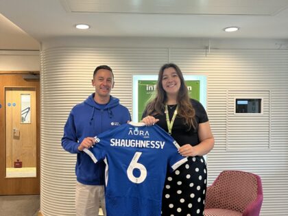 a photo in a reception area of a man and woman holding as Pompey Football club shirt, worn by Portsmouth football player Connor Shaughnessy