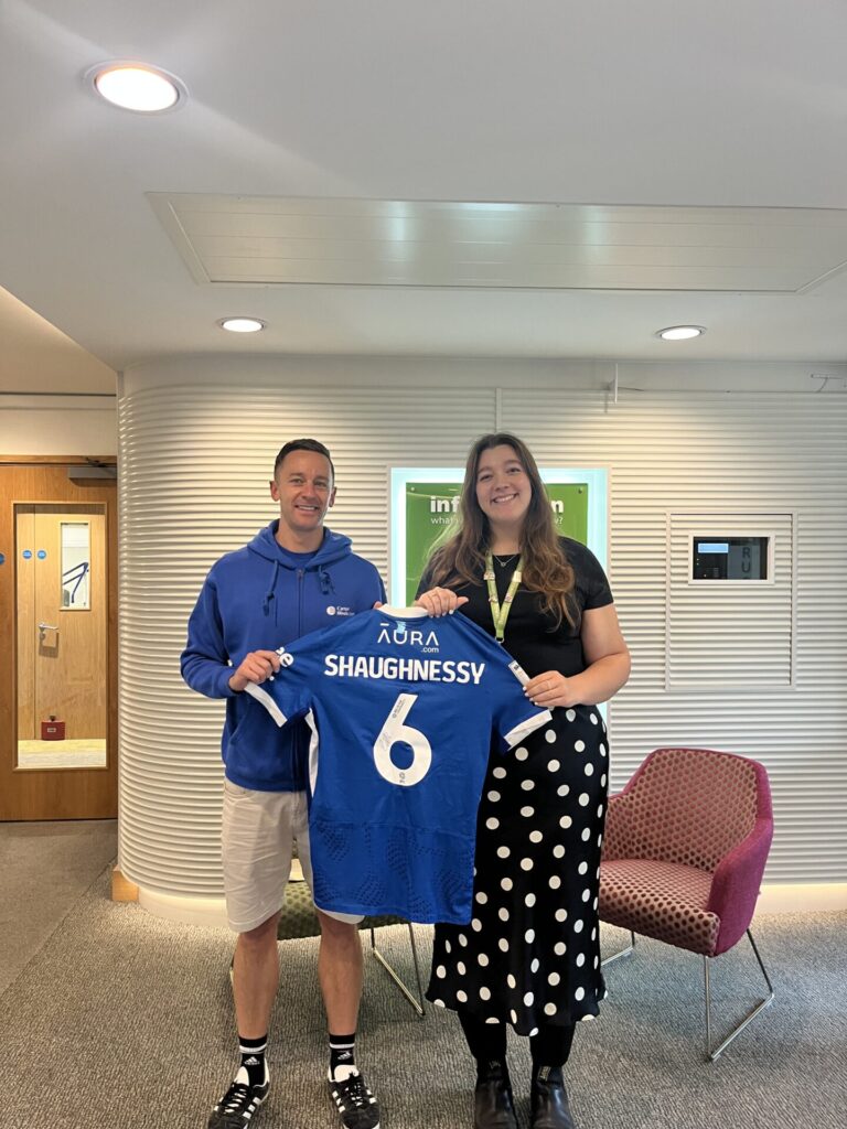 a photo in a reception area of a man and woman holding as Pompey Football club shirt, worn by Portsmouth football player Connor Shaughnessy