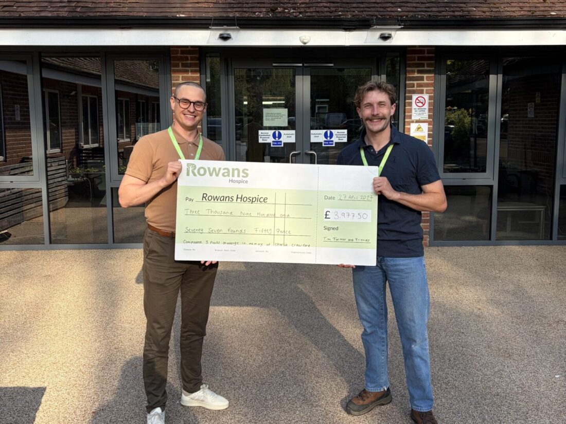 photo of two men outside rowans hospice building holding a cheque and smiling at the camera after raising money for the charity