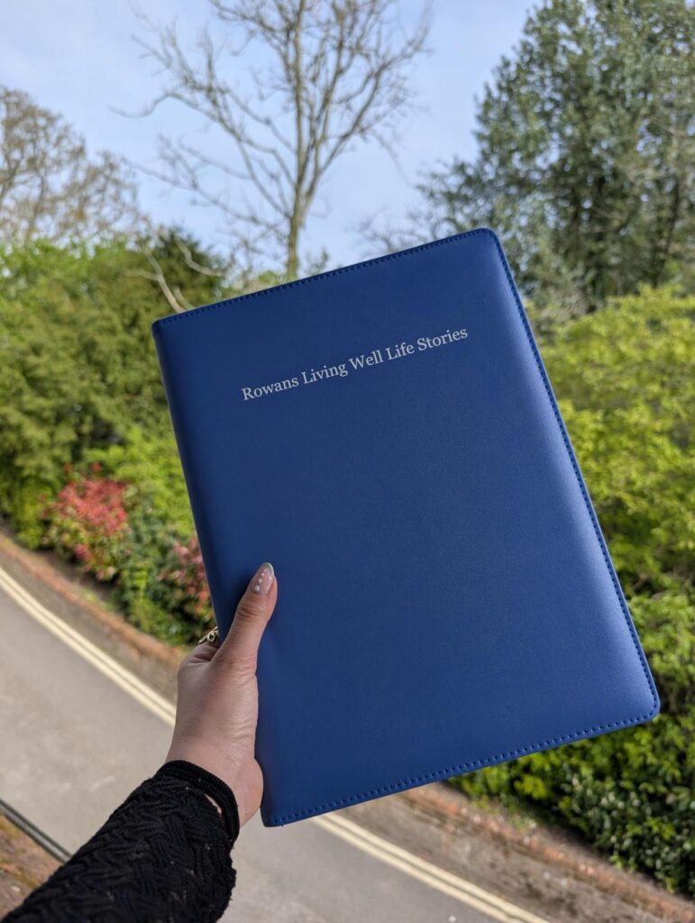 Blue book reading Life Story Living Well Services with colourful sky and green forest background