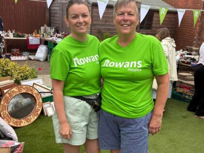 photo of two ladies wearing green rowans hospice t shirts in their garden sale with bunting and tables of items