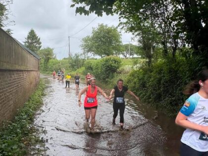 a muddy trail with a muddy puddle and ladies in running gear running through smiling