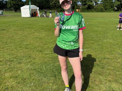 photo of a girl in a green rowans running top stood on a field with a hat and holding a medal after running a marathon
