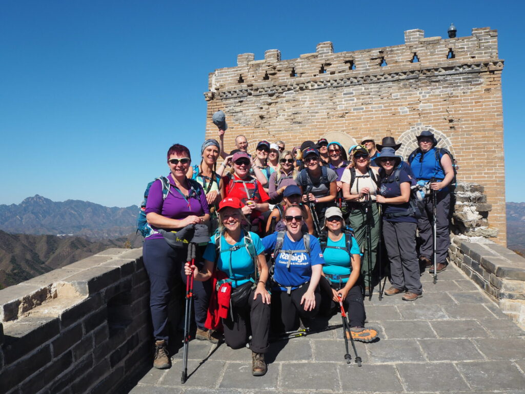 Group of people in hiking gear in front of part of the great wall of china.