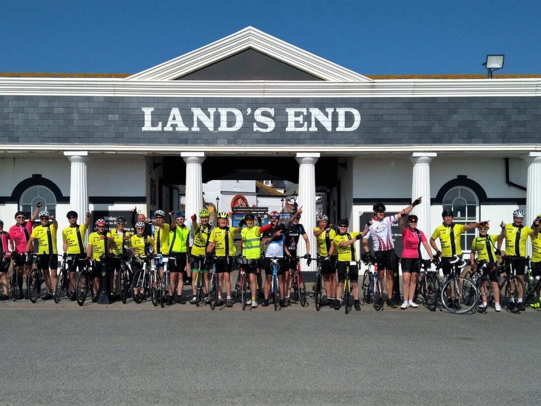 group of cyclists in front of building with "Land's end" sign on
