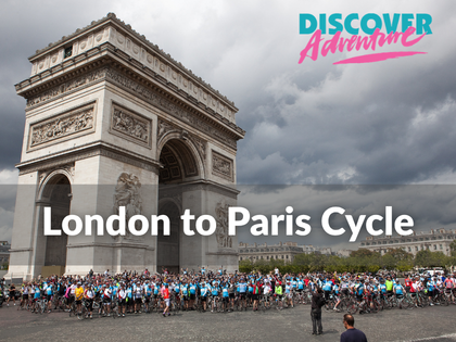 Wide photo of crowd of cyclists with their bikes in front of Arc de Triumph in Paris. The skies over the photo are grey and cloudy. ~Over the photo is text "London to Paris Cycle" and Discover Adventure's logo