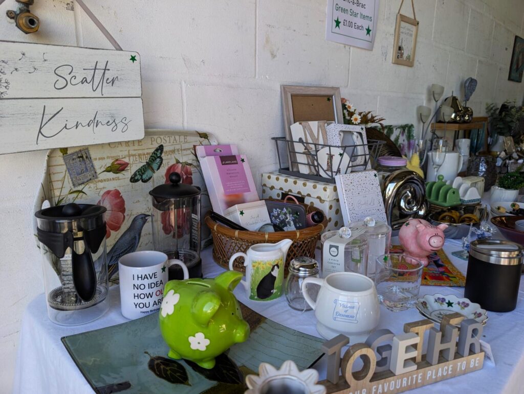 Table with scattered bric a brac items, including a green pig money pot, a home sign, mugs and coasters